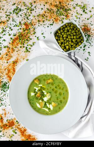 Von oben pürierte Gemüse cremige Suppe mit kleinen Crackern und Grüne Erbsen in weißer Schale auf Holzhintergrund Stockfoto