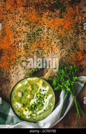 Von oben pürierte Gemüsesuppe mit kleinen Kräckern, Petersilie und grünen Erbsen auf Pfanne auf Holzgrund Stockfoto