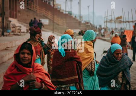 Allahabad, Indien - FEBRUAR, 2018: Gruppe von älteren armen indischen Frauen in typischen bunten Kleidern mit Schals auf Köpfen zu Fuß auf Flussufer neben dem Hafen im Dorf Stockfoto