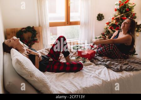 Zwei schöne Freunde lachen im Bett zu Hause in der Nähe weihnachtsbaum in gemütlichen Innenraum. Innenausstattung mit weihnachtsdekorationen. Stockfoto