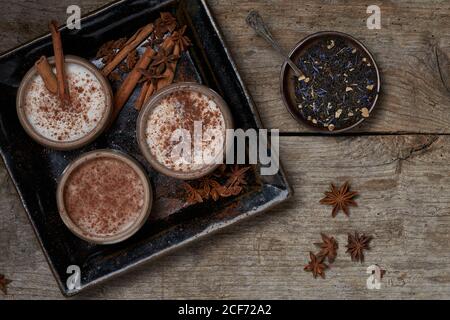 Draufsicht auf Masala Chai serviert in Keramikschalen mit Sternanis und Zimtstangen auf Holztisch mit angeordnet Teekanne und ein Stück Tuch Stockfoto