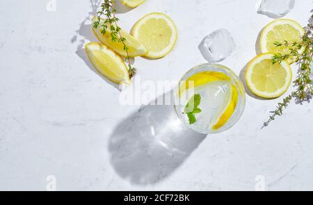Von oben Gläser mit erfrischendem kaltem Thymian und Ingwerlimonade Mit Scheiben Zitronen- und Minzblätter auf dem Tisch serviert In hellem Raum Stockfoto