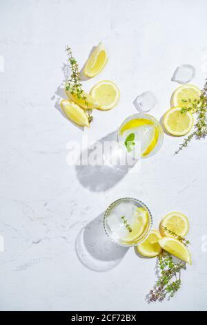 Von oben Gläser mit erfrischendem kaltem Thymian und Ingwerlimonade Mit Scheiben Zitronen- und Minzblätter auf dem Tisch serviert In hellem Raum Stockfoto