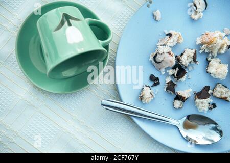 Von oben leerer grüner Keramikbecher auf Untertasse gefallen und Blauer runder Teller mit kleinen Krümeln von leckerem Gebäck Zusammensetzung mit schmutzigem Metall Teelöffel nach dem Frühstück Stockfoto