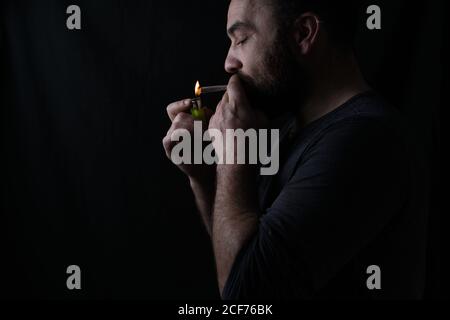 Seitenansicht der Ernte konzentrierte männliche Raucher Beleuchtung Marihuana Stumpf auf schwarzem Hintergrund Stockfoto