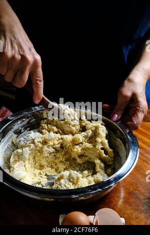 Von oben anonymen Menschen mit Holzlöffel, weich zu mischen Teig in Metallschüssel auf Tisch in der Küche Stockfoto