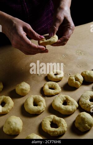 Anonyme Frau, die Ringe aus weichem Teig macht, während sie in der Küche Donuts über dem Tisch zubereitet Stockfoto