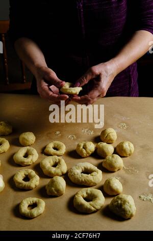 Anonyme Frau, die Ringe aus weichem Teig macht, während sie in der Küche Donuts über dem Tisch zubereitet Stockfoto