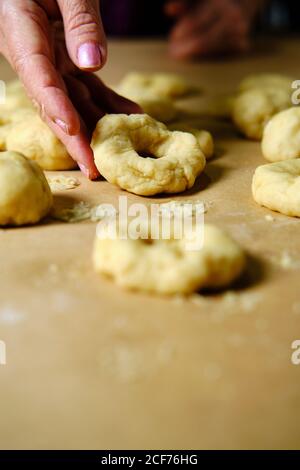 Anonyme Frau, die Ringe aus weichem Teig macht, während sie in der Küche Donuts über dem Tisch zubereitet Stockfoto