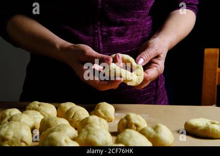 Anonyme Frau, die Ringe aus weichem Teig macht, während sie in der Küche Donuts über dem Tisch zubereitet Stockfoto