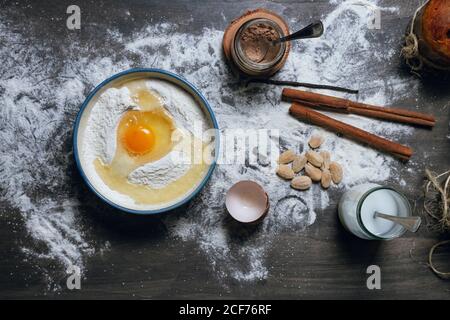 Draufsicht der Zutaten für Panettone Rezept einschließlich Schüssel mit Mehl und Ei und Gläser mit Kakaopulver und Milch Auf einen gestaubten Tisch mit Mandeln und Gewürzen gestellt Stockfoto