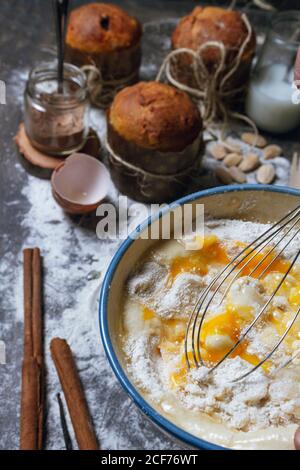 Hausfrau mit Schneebesen Mischen von Produkten in Keramikschale während der Vorbereitung Teig für typische Weihnachten Panettone Kuchen auf dem Tisch mit gebacken Panettone und Zutaten Stockfoto