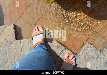 Frauenfüße in Sandalen und der alte Stadtbrunnen Stockfoto