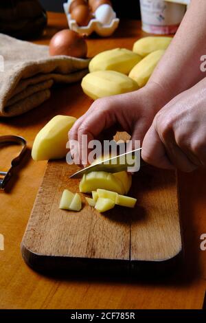 Crop anonymous kochen Schälkartoffel über Holz Schneidebrett in Moderne Küche Stockfoto