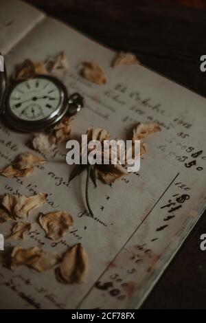 Blütenblätter aus getrockneter Rose und Vintage-Taschenuhr platziert auf Schäbige Seite eines alten Tagebuchs mit Erinnerungen Stockfoto