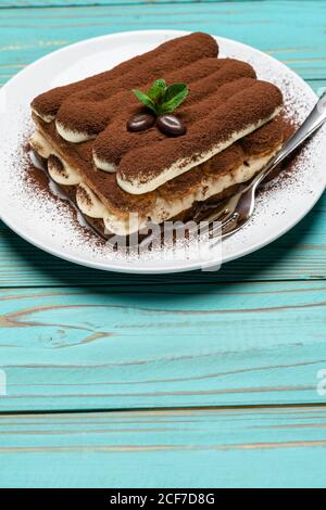 Portion Classic Tiramisu Dessert auf Keramikplatte auf bunt Blauer Holzhintergrund Stockfoto