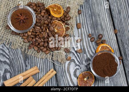 Kaffeebohnen auf grober Bettwäsche. Gemahlener Kaffee in Behältern und Gewürzen. Auf einer Oberfläche aus gebürstetem Kiefernholz, schwarz und weiß lackiert. Stockfoto