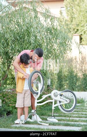 Liebevoller Vater und sein Sohn verbringen Zeit zusammen im Freien Reparatur Fahrrad an sonnigen Tag, vertikale Aufnahme, Kopierraum Stockfoto