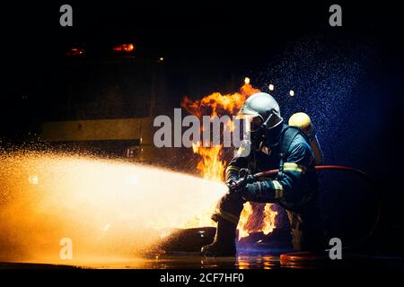 Nicht erkennbarer Mann in Feuerwehruniform unterdrückt Feuer mit schweren Strom Von Wasser Stockfoto
