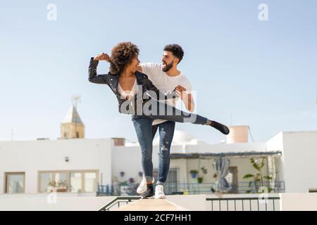 Multirassische Männer und Frauen lachen und balancieren an der Wand, während sie während des Datums auf der Stadtstraße Spaß haben Stockfoto