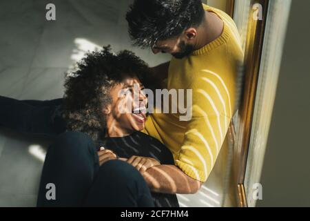 Ziemlich fröhliche afroamerikanische Frau, die lachend auf den Knien eines bärtigen Mannes in einem stilvollen Zimmer lag Stockfoto