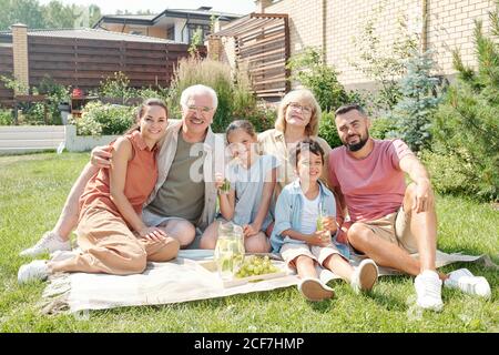 Portrait der großen Multi-Generation-Familie sitzen auf Rasen im Hinterhof an sonnigen Sommertag, Blick auf die Kamera Stockfoto