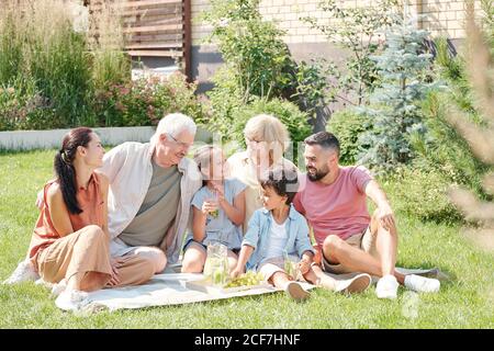 Portrait der fröhlichen Multi-Generation-Familie auf Rasen im Hinterhof sitzen Am sonnigen Sommertag Picknick Stockfoto