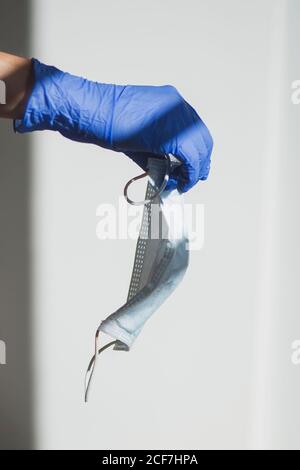 Crop anonyme Person in blauen Latex-Handschuh hält medizinische Maske Vor weißem Hintergrund, der das Konzept des Coronavirus-Schutzes und der Prävention darstellt Stockfoto