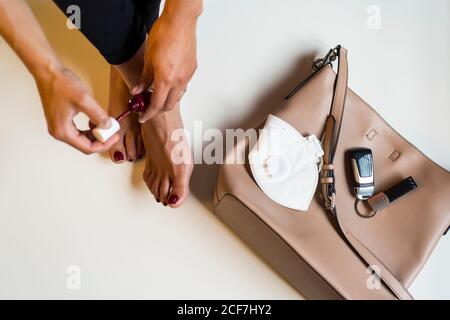 Von oben der Ernte anonyme weibliche Herstellung Pediküre und Anwendung Nagellack beim Sitzen in der Nähe der Handtasche mit Schutzmaske und Fahrzeugschlüssel Stockfoto