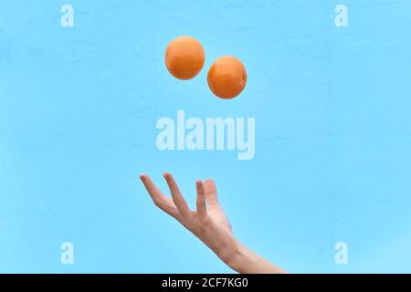 Crop Frau wirft frische Orange in Luft zeigt Konzept der gesunden Ernährung auf blauem Hintergrund Stockfoto