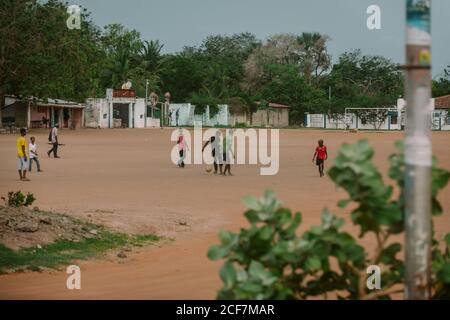 Gambia, Afrika - 5. August 2019: Schwarze arme Jungen spielen Fußball mit Vergnügen auf dem Boden in geräumigen Bezirk tagsüber Stockfoto