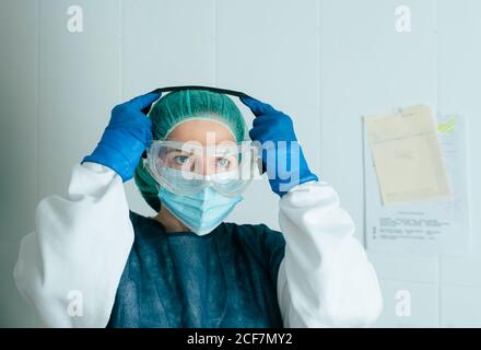 Junge weibliche Sanitäter in Schutzkleidung und Maske anziehen Brille während der Arbeit im Krankenhaus während einer Coronavirus-Pandemie Stockfoto