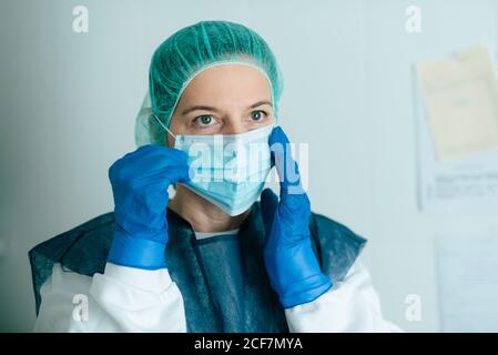 Junge weibliche Sanitäter in Schutzkleidung und Maske anziehen Brille während der Arbeit im Krankenhaus während einer Coronavirus-Pandemie Stockfoto