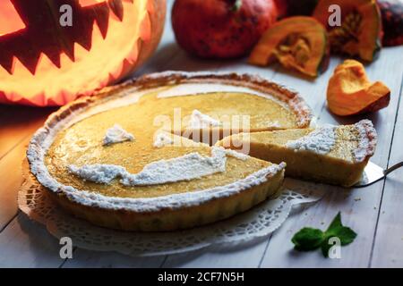 Köstliche hausgemachte Kürbis halloween Kuchen mit geschnitzten Jack-o-Laterne auf dem Hintergrund. Orangenkuchen mit Minze und Zuckerpulver. Food-Fotografie Stockfoto