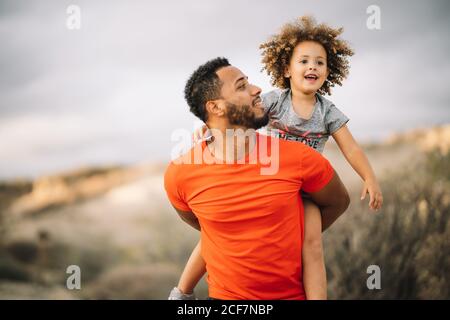 Lächelnder afroamerikanischer bärtiger Mann in sportlicher Kleidung Fröhliches lockiges aktives Kleinkind beim Wandern in der Natur Stockfoto