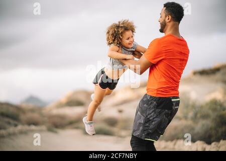 Lächelnder afroamerikanischer bärtiger Mann in sportlicher Kleidung Fröhliches lockiges aktives Kleinkind beim Wandern in der Natur Stockfoto