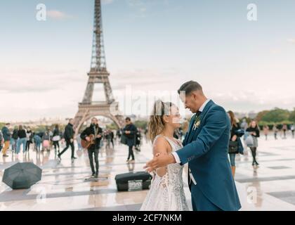 Bräutigam im blauen Anzug und Braut im weißen Hochzeitskleid Langsamer Tanz lächelnd und einander anblickend Eiffelturm im Hintergrund bei Paris Stockfoto