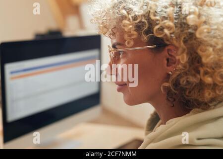 Nahaufnahme von reifen Frau mit lockigen Haaren in Brillen suchen Am Computermonitor Stockfoto