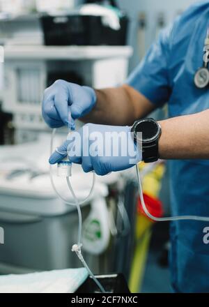 Crop männliche Hände in blauen Gummihandschuhe Vorbereitung Medizin für Infusion im Krankenhaus auf verschwommenem Hintergrund Stockfoto