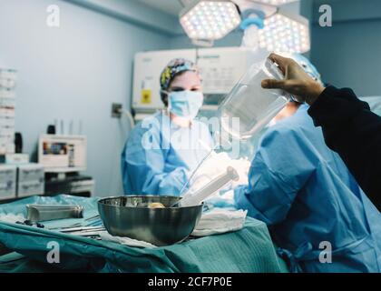 Schneiden Sie die Hand Gießen Kochsalzlösung in die Schüssel mit Spritze während Ärzte machen Chirurgie im Operationssaal Stockfoto