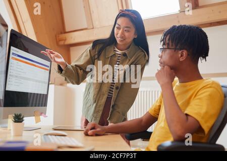 Asiatische junge Frau zeigt auf Computer-Monitor und diskutieren mit Ihre Kollegin hat neue Software, während sie im Büro arbeitet Stockfoto