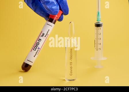 Crop anonyme Arzt in Latex-Handschuhe halten Reagenzglas mit Blutprobe des Patienten mit Coronavirus-Infektion in der Nähe von Ampulle mit Impfstoff und Spritze Stockfoto
