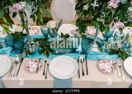 Von oben der Hochzeitstisch mit blau und beige dekoriert Tuch und Blumen Blumensträuße in hohen Vasen und serviert mit Porzellanteller und blaue Gläser Stockfoto