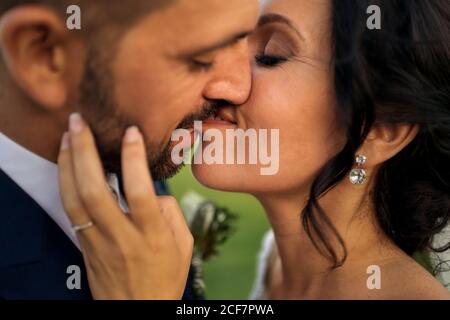 Seitenansicht des fröhlichen Bräutigams im eleganten Smoking Lifting Braut Im Hochzeitskleid, während Sie auf der tropischen grünen Küste in stehen Abends Stockfoto