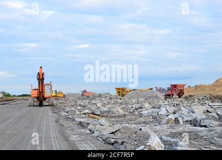 Bagger mit einem hydraulischen Hammer und Schere zerstört die Fahrbahn und Bürgersteig. Mobile Steinbrecher-Maschine von der Baustelle für Crushin Stockfoto