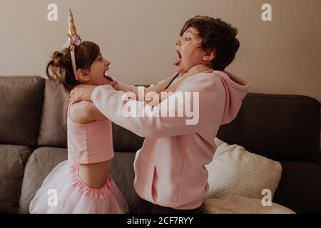 Seitenansicht von Bruder und Schwester in rosa Outfits würgen Einander beim Kämpfen in der Nähe von Sofa zu Hause Stockfoto