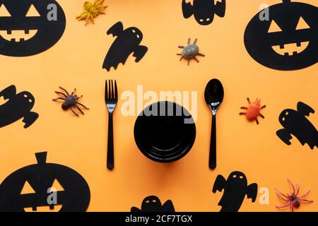 Flacher Halloween Hintergrund mit schwarzem Geschirr, dekorativen Spinnen und Gespenst auf orangefarbenem Hintergrund. Platz für Text kopieren. Einladung zum festlichen Abendessen. Stockfoto