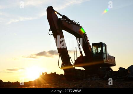 Raupenbagger mit Hydraulikhammer bei Sonnenuntergang. Zerstörung, Abriss von Beton und Hartgestein auf der Baustelle oder im Steinbruch. Jackh Stockfoto