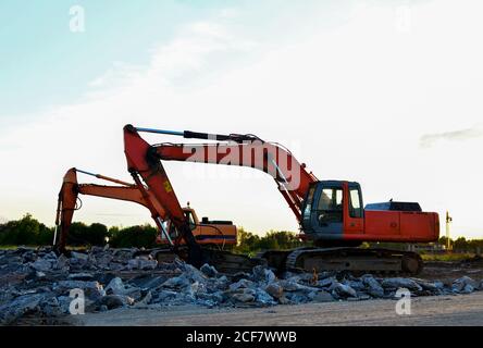 Raupenbagger mit Hydraulikhammer bei Sonnenuntergang. Zerstörung, Abriss von Beton und Hartgestein auf der Baustelle oder im Steinbruch. Jackh Stockfoto
