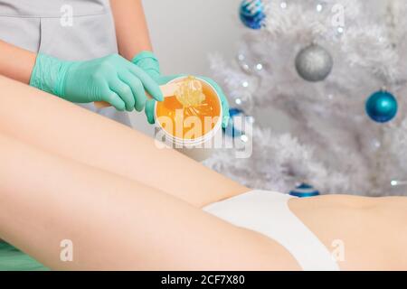 Junge Frau bekommt Wachs Epilation der Beine. Enthaarungskonzept. Produkt Wachsschale. Weihnachtsrabatt wachsen Stockfoto